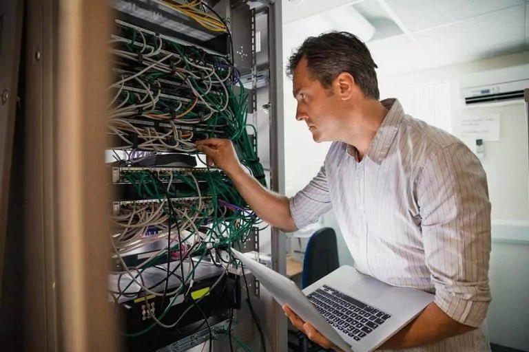 Technician working in a server cabinet with laptop in hand.