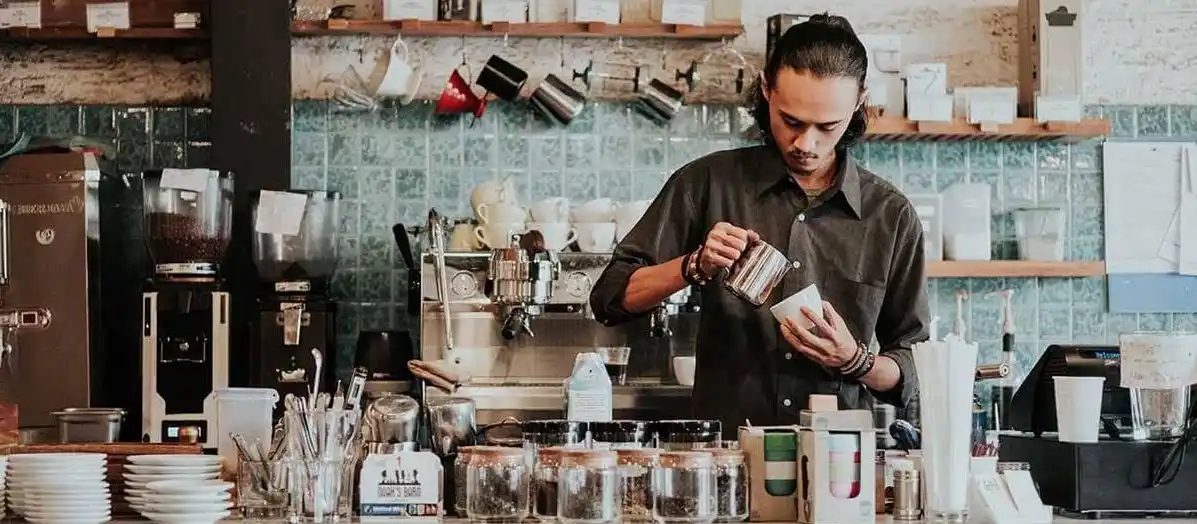 A man stands behind the counter of a coffee shop, ready to serve customers.