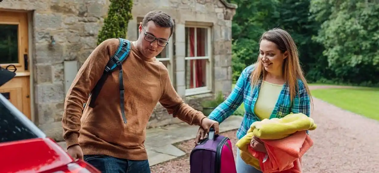 A man and woman stand by a car, holding luggage as they prepare to travel.