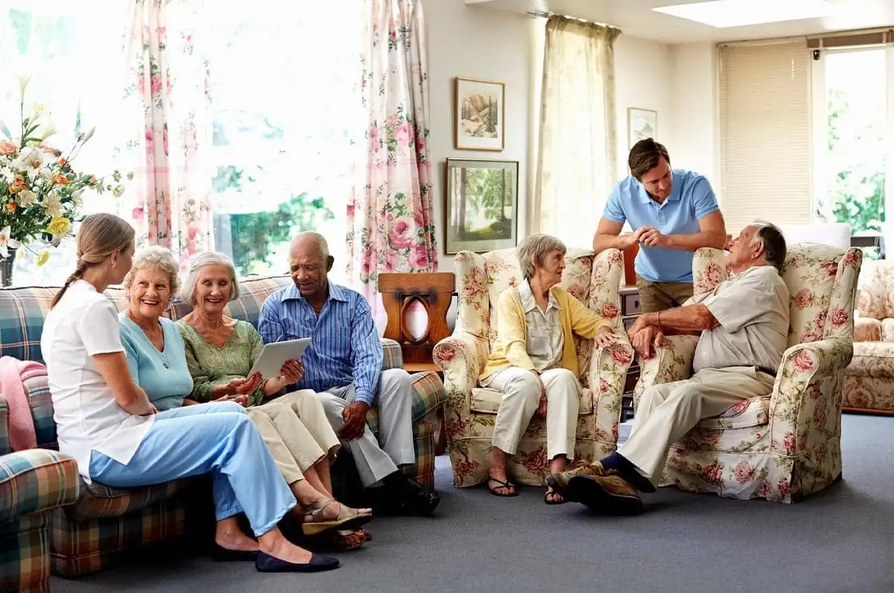 Several elderly people gathered in a care home, sitting comfortably and sharing stories in a warm, inviting atmosphere.