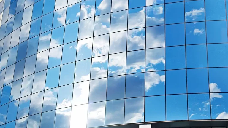A modern building with glass walls reflecting the sunlight and a partially cloudy sky above.