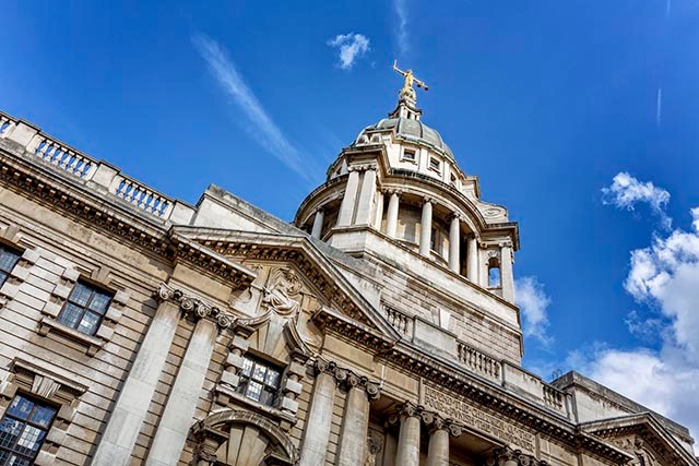 Exterior of a court building with stone columns viewed from a low angle. Lady Justice statue is at the top of a dome.