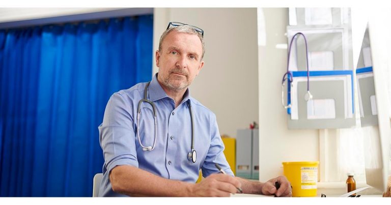 Doctor with stethoscope around his neck sitting at a desk in a medical office.