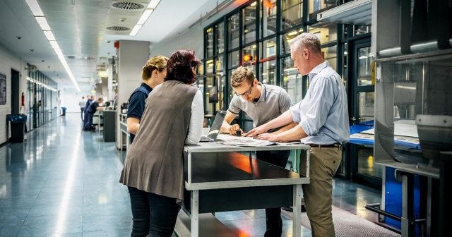 People gathered around a table discussing documents in an industrial office during a commercial manufacturing meeting.