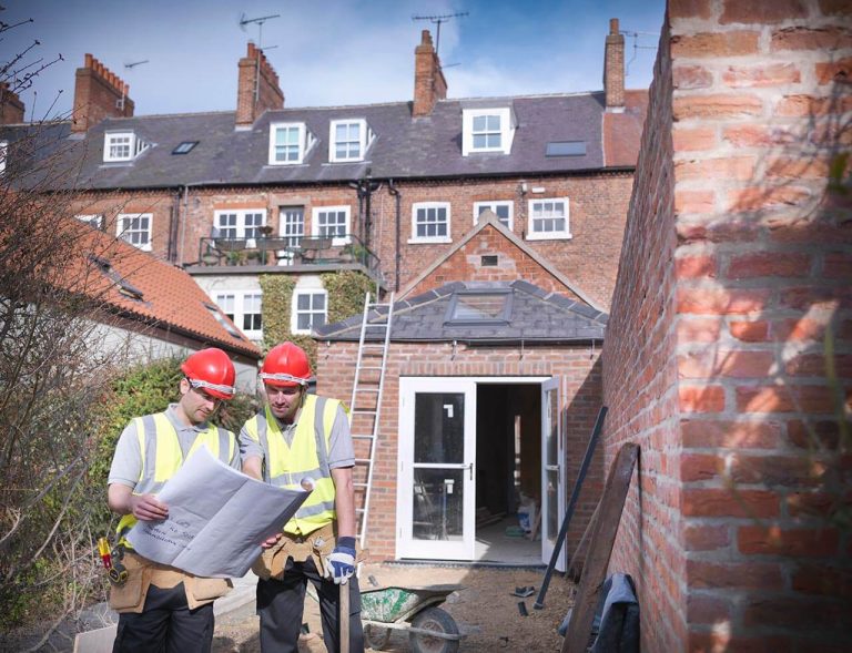 Two construction workers examining blueprints at a residential brick building site.