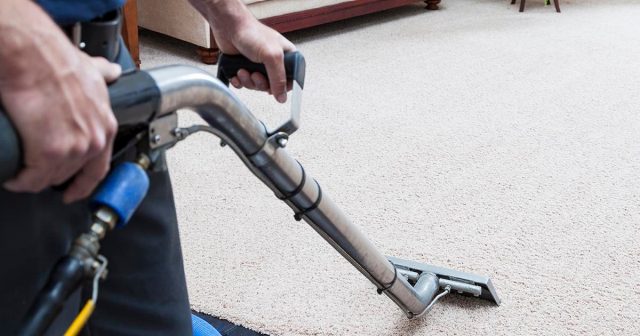Person using a carpet cleaning machine on a light-coloured carpet.