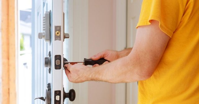 Person using a screwdriver to adjust a lock on a white door with multiple locks and keypad.