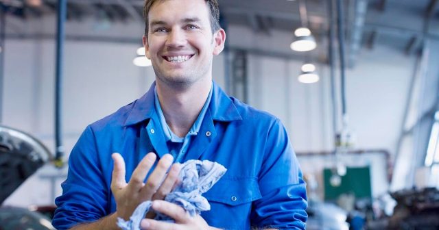 Mechanic smiling while holding a blue cloth in an auto repair shop.