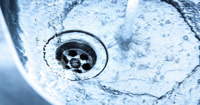 Water flowing into a stainless steel sink, swirling around the drain.