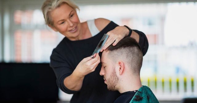 Hairstylist cutting a man's hair in a hair salon, using scissors and a comb.