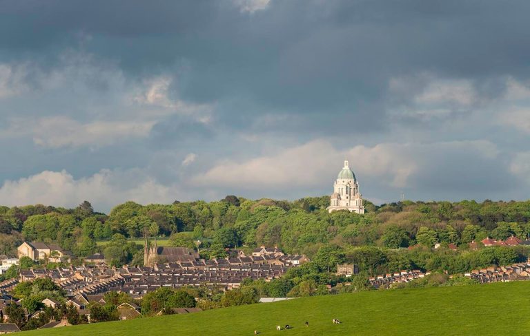 View of Lancaster with Ashton Memorial and grassy field, under a cloudy sky.