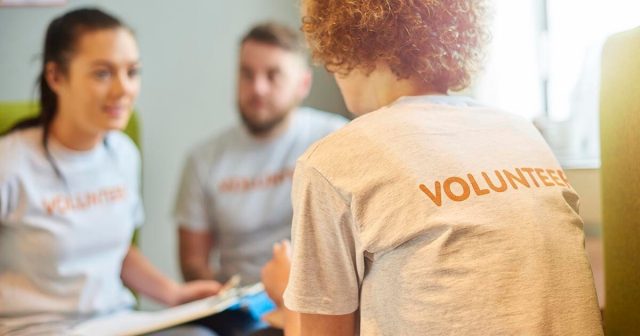 Three people in a discussion indoors, one with "Volunteer" on their back.
