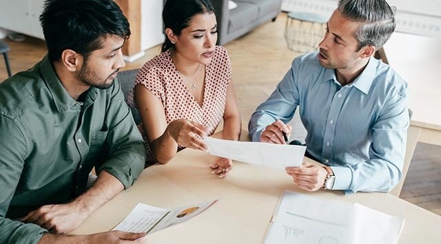 Three people in a professional indemnity meeting, discussing documents around a table.