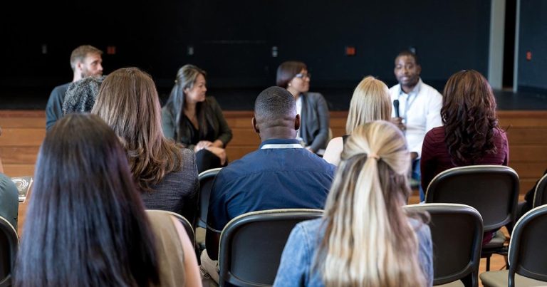 Audience at a sports community centre, facing a panel of four individuals.