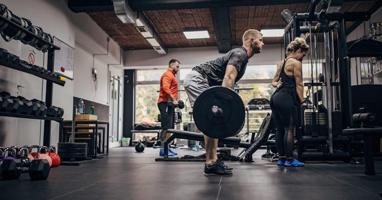 Three people working out in a gym with deadlifts, cable machines, and kettlebells.