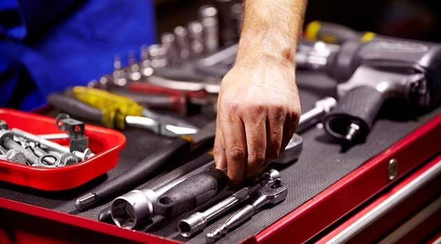 Hand selecting tools from a chest, with bolts, wrenches, and power tools visible.