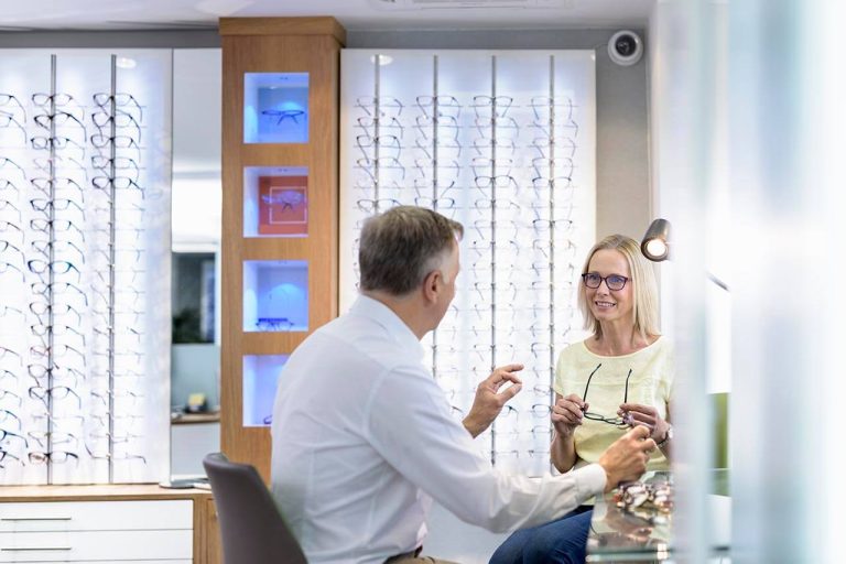 Woman holding glasses while consulting with an optician in an eyeglass shop.
