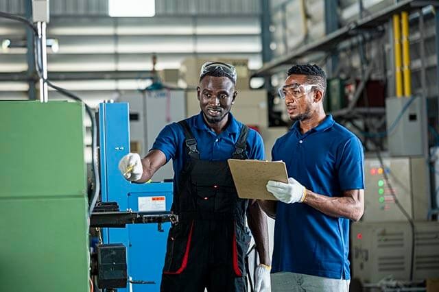 Two men discussing an engineering task in a manufacturing workshop with safety gear on.