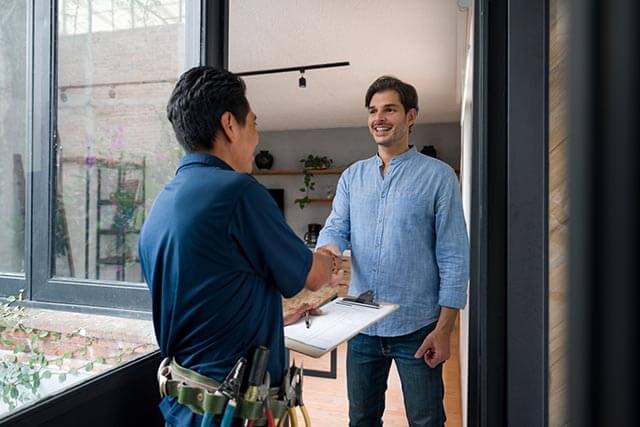 Contractor shaking hands with a customer outside a house, both smiling in a friendly, professional exchange.