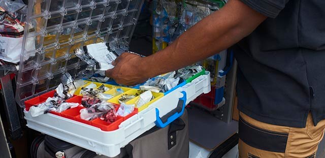 Electrician organising electrical components in a sectioned toolbox with various items.