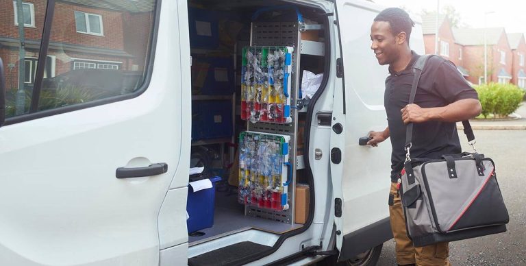 Trade worker beside an open van door, with tools and stock visible in the van, smiling with houses in the background.