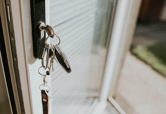 Keys inserted into a door lock, with green grass visible outside.