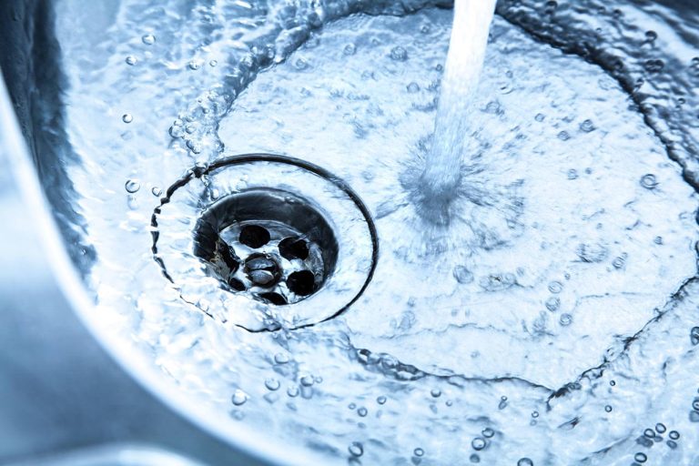 Water flowing from a faucet into a stainless steel sink with ripples and bubbles.