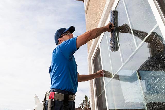 A window cleaner in uniform, cleaning a window with a squeegee.