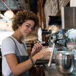 A woman prepares coffee behind the counter in a coffee shop.