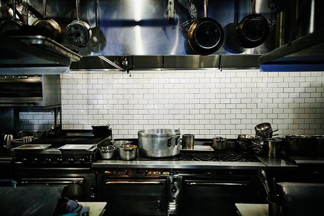 Professional kitchen with stainless steel equipment, including ovens, counters, and ventilation hoods.