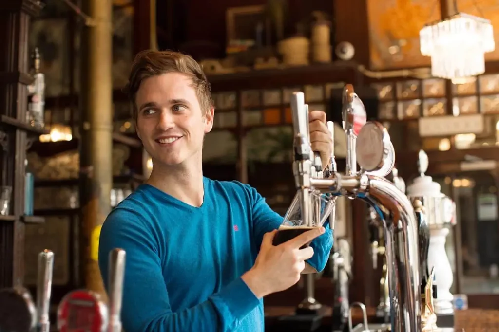 Bartender pouring a pint behind a bar in a pub.