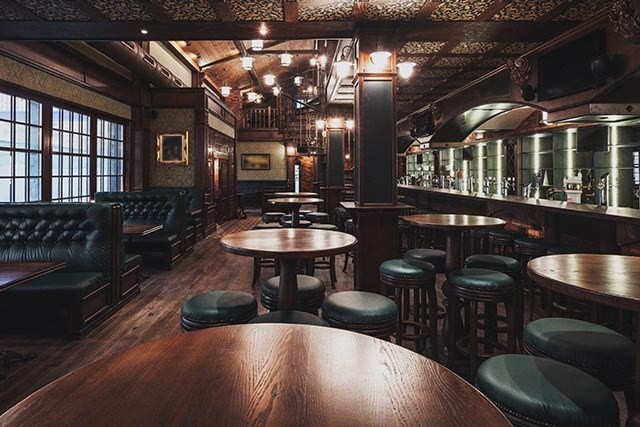 Interior of a bar showcasing rustic wooden tables and stools, with a warm and inviting atmosphere.