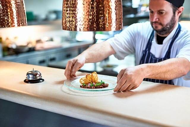 Chef placing a plated dish on a counter with crispy food garnished with greens.