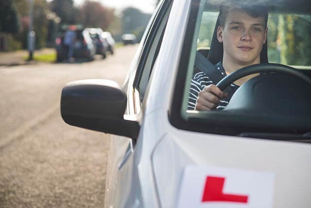 Learner driver with an L-plate driving on a residential street.