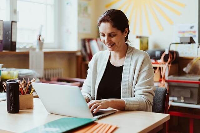 A person typing on a laptop at a desk, with a pencil case and a drink on the desk.