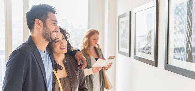 Couple smiling and looking at framed pictures in an art gallery.