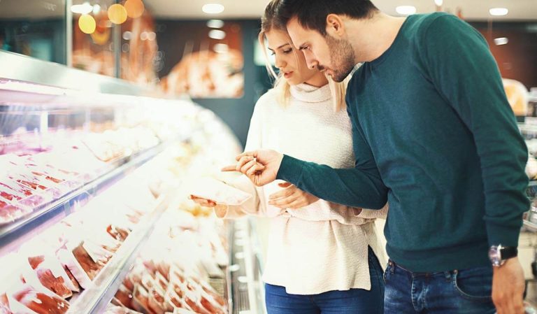 Man and woman examining packaged meat in a grocery store with a refrigerated display.