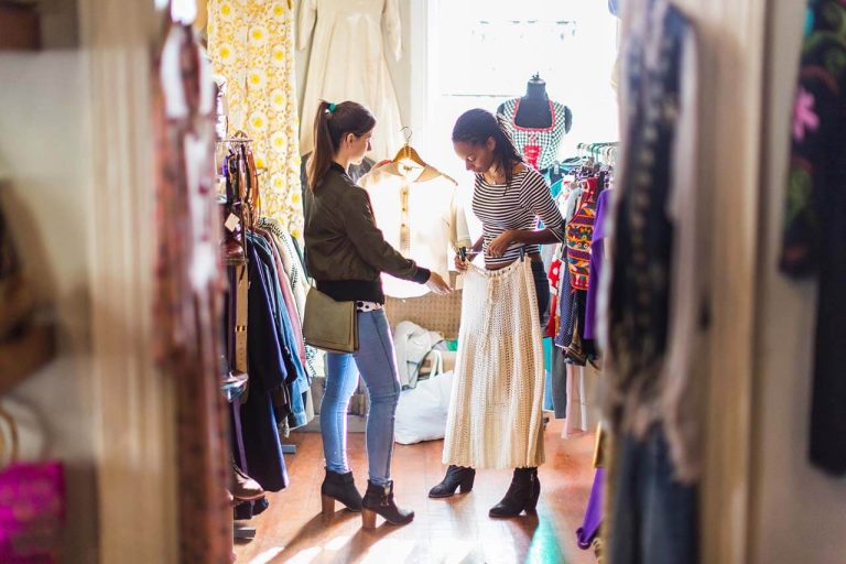 Two friends browsing clothes in a store, inspecting a beige skirt.