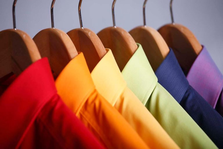 Colourful collared shirts hanging on wooden hangers against a plain background.