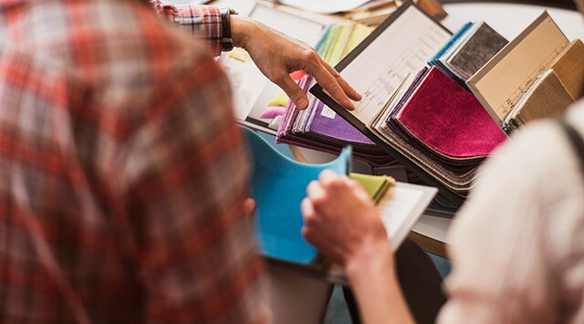Two people examining fabric swatches and documents at a furniture shop, with colorful fabric on the table.