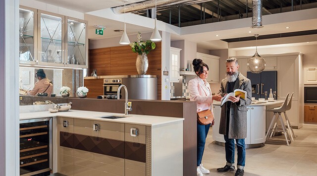 A man and woman discussing a brochure in a modern kitchen showroom with sleek cabinets and industrial elements.