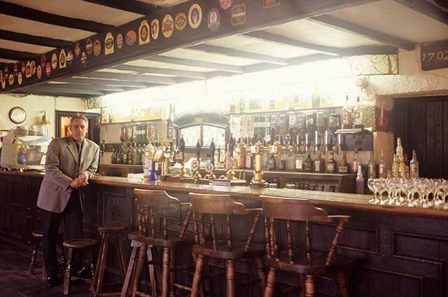 Man in a suit stands by a wooden bar in a sports social club.