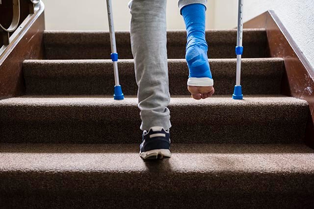Person with blue cast on crutches ascending a staircase, wearing sweatpants and a trainer on their left foot.