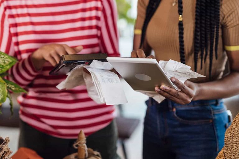 Close up or two people holding receipts and looking at a tablet device