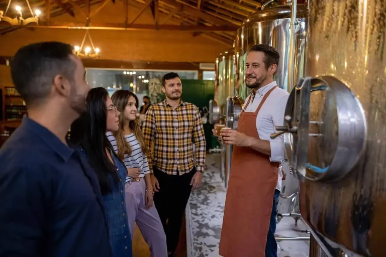 Group of five people on a guided tour inside a brewery, standing near large stainless steel brewing tanks.