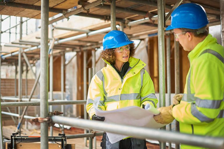 Two workers discussing scaffolding plans at a construction site surrounded by scaffolding.