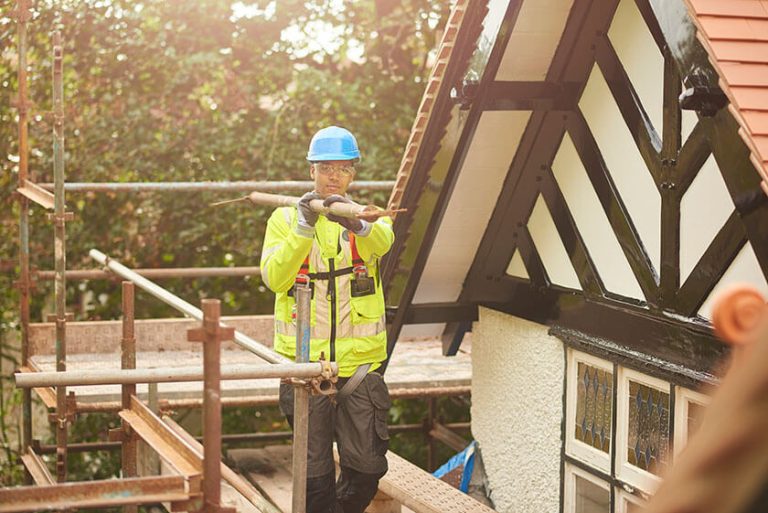 A construction worker carrying a metal pole on scaffolding beside a building.