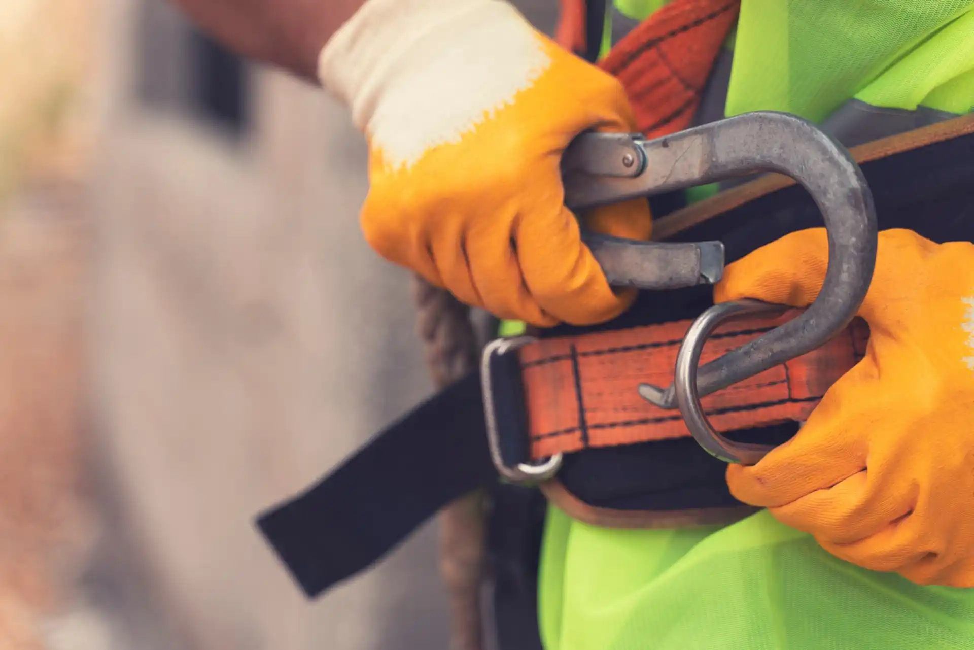 A worker wearing a safety harness, fastening a hook onto the harness belt to ensure construction site safety