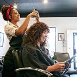 A hairstylist trims a woman's hair, showcasing a professional salon environment.