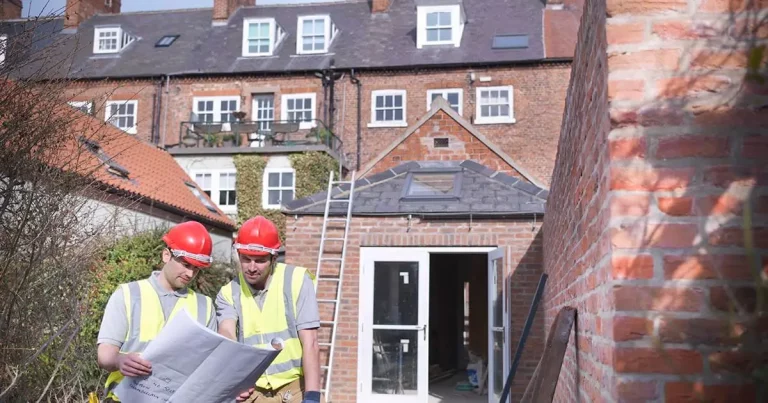 Two construction workers examining blueprints at a residential brick building site.